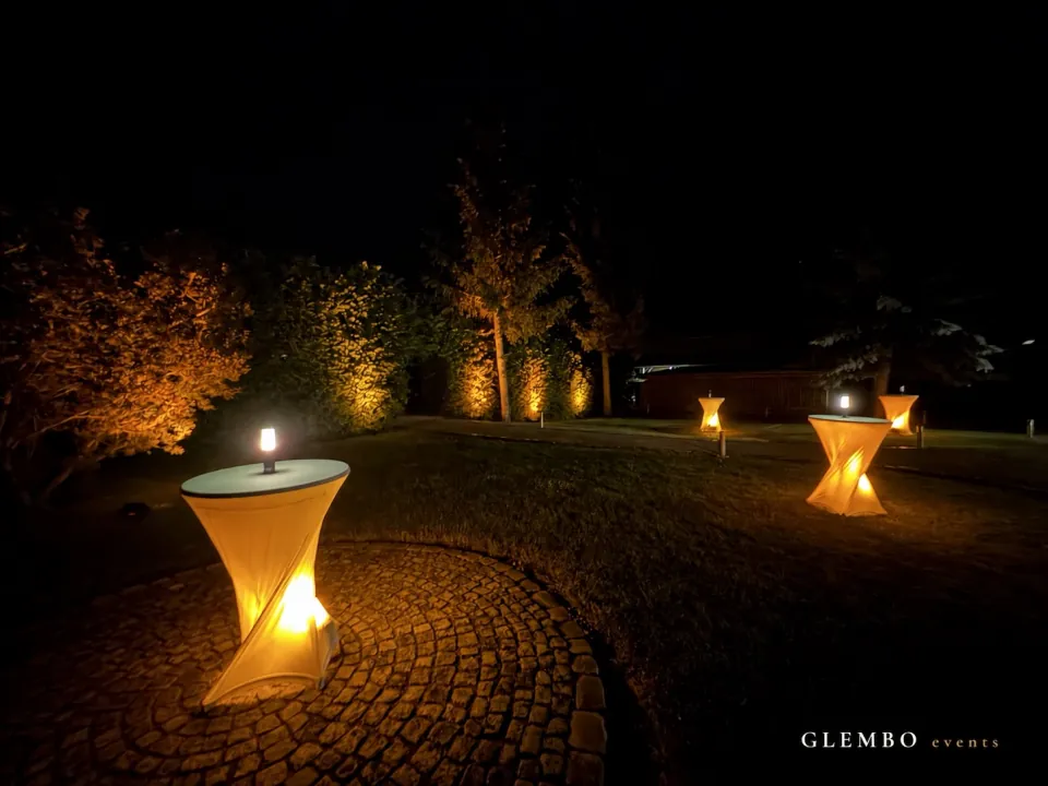 Unterleuchtete Stehtische und mit Uplights illuminierte Hecken im Außenbereich des Landkulturhofs Glücksbringer