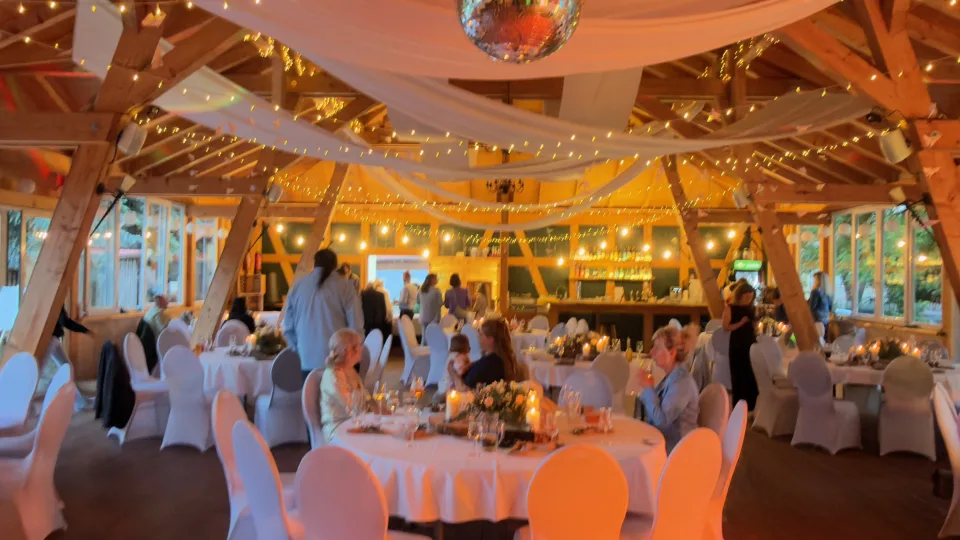 Festlich für eine Hochzeit eingedeckte Festscheune im Landkulturhof Glücksbringer mit Lichterketten und warmem Ambientelicht