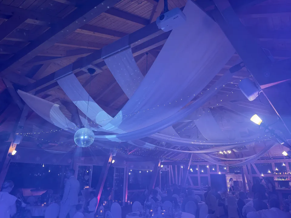 Tanzende Hochzeitsgäste unter Lichterketten und Discokugel in der Festscheune des Landkulturhofs Glücksbringer in blauem Licht